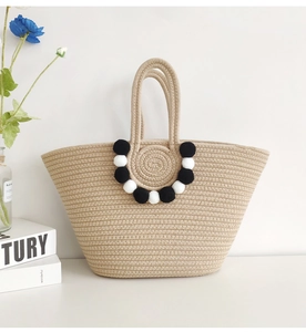 Detail of handmade woven straw tote bag with black and white pom-pom bead charms