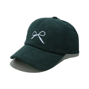 Detailed close-up of dark green corduroy cap with white bow embroidery and texture