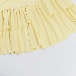 Detail of light yellow tiered ruffles and pleated hemline on high-waisted mini skirt