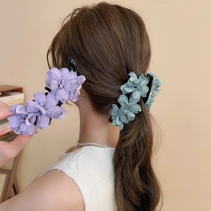 Vue détaillée de pinces à cheveux à fleurs en tissu élégantes en violet et bleu sur un chignon
