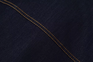 Gros plan du tissu denim bleu foncé avec des coutures contrastées orange et texture sergé
