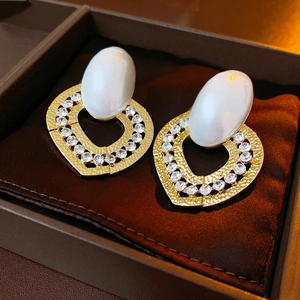 Macro detail of luxury heart-shaped gold earrings with pearls and crystals in a box