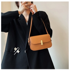 Close-up of a brown leather shoulder bag with gold rectangular buckle on a model suit