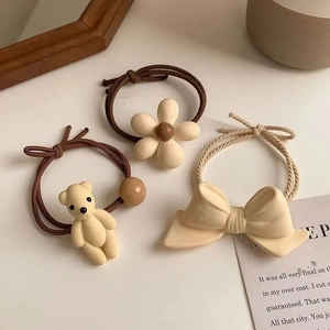 Detail of 3-piece hair tie set featuring beige bow, brown bear and floral charms