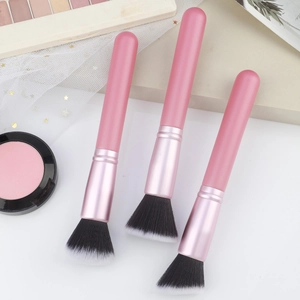 Detailed view of three soft fiber makeup brushes with pink handles on a makeup tray