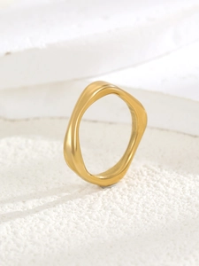 Detail of minimalist wavy gold ring with organic curves on textured white background