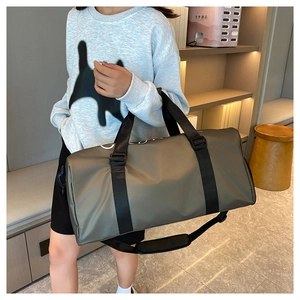 Side view of large grey waterproof nylon duffle bag worn by model in a travel setting