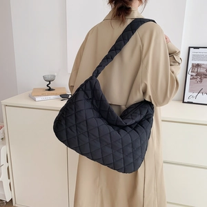 Quilted black hobo bag with thick woven strap shown with beige trench coat in a lifestyle setting