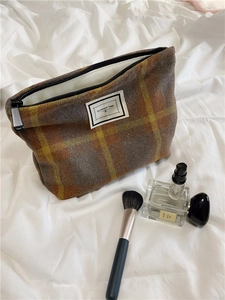 Detail of plaid wool cosmetic bag with Pleasant Time label on soft white fabric background