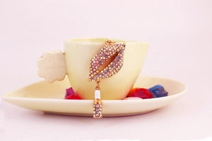 Detail of red lips and lipstick keychain charm with rainbow rhinestones on a cup