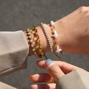 Dettaglio di bracciali a strati in oro 18K e acciaio con croce, perle e zirconi