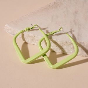 Detail of large green square hoop earrings resting on natural stone with soft lighting