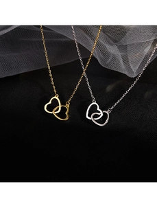 Close-up of interlocking gold and silver heart pendants on delicate chains over black silk