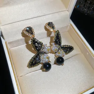 Luxurious butterfly drop earrings with black stones and pearls on a silk jewelry display