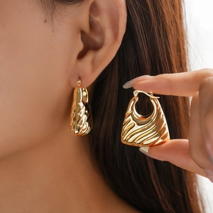Detail of gold geometric earrings featuring a textured square pattern on a trapezoid shape