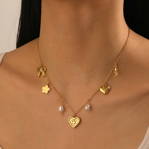 Detail of gold necklace with charms like bow, heart with crown, pearl, and star