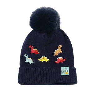 Detail of navy knit kids beanie with colorful dinosaur embroidery and a faux fur pompom
