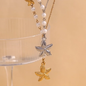 Detailed shot of asymmetric two-tone starfish charms and white pearl on gold silver necklace
