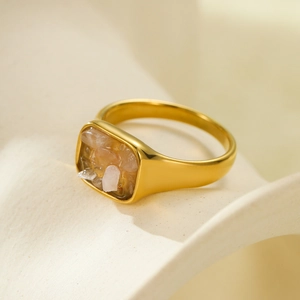 Macro shot of gold square ring inlaid with pink and orange natural stones on beige surface