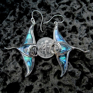Orecchini a forma di manta con inserto iridescente e moneta di riferimento su roccia