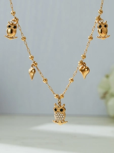 Detail of gold necklace with zircon owl pendants and heart charms on a beaded chain