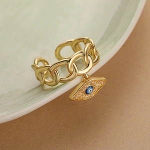 Gold adjustable chain ring with a blue evil eye pendant and zircon accents on a ceramic bowl