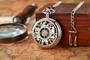 Close-up of vintage silver compass pocket watch with intricate hollow design on antique map