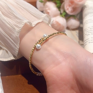 Detail of beaded gold bracelet with two white pearls on female wrist with floral background