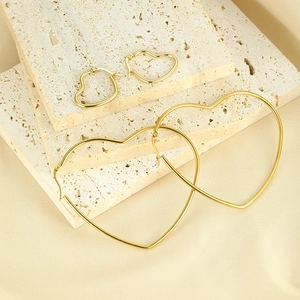 Macro shot of two pairs of gold heart hoop earrings in different sizes on travertine