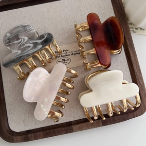 Detail of four acetate hair claws in marble and amber textures on a wooden display tray