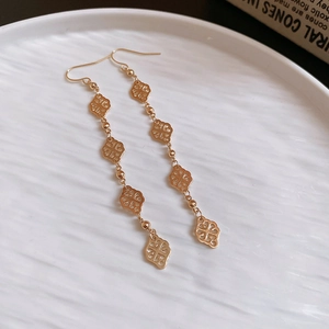 Détail de boucles d'oreilles pendantes dorées avec motifs trèfles et perles en métal