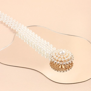 Detail of white pearl waist belt with gold rhinestone buckle on a reflective surface