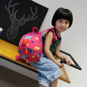 Pink cartoon dinosaur toddler backpack with 3D orange spines on girl sitting on bench