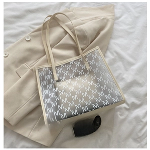 Detail of large beige tote bag with letter patterns showing size compared to a phone