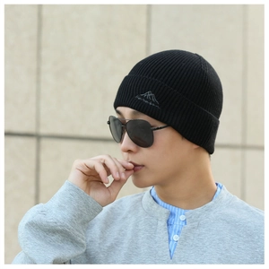 Close-up of black knit beanie with mountain embroidery worn by male model