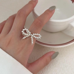 Close-up of 925 sterling silver bow knot beaded open ring on finger with gray manicure