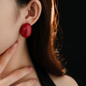 Close-up of a model wearing large red oval stud earrings with a glossy enamel finish