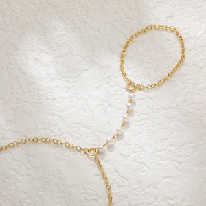 Detailed view of golden hand chain bracelet with white pearls and finger ring connector
