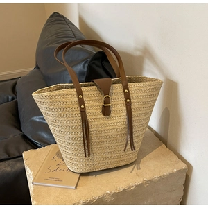 Detail of straw woven tote bag with brown leather handles and gold buckle closure