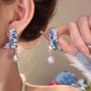 Silver butterfly earrings with blue crystals and a teardrop pearl pendant on a model