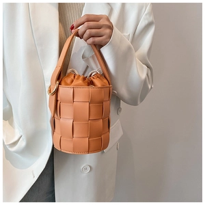 Detail of a vibrant orange woven bucket bag with a beige drawstring lining held by a model