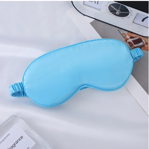 Close-up of light blue silk sleep mask with elastic strap on white fabric background