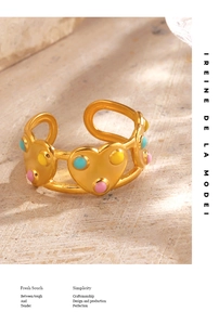 Détail d'une bague coeur dorée avec points en émail colorés sur fond de pierre