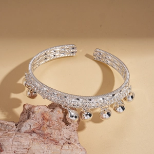 Détail d'un bracelet ouvert argenté avec de petits grelots suspendus sur un support minéral