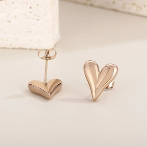 Macro view of 18K gold plated heart stud earrings on a light stone background