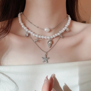 Detail of layered beach necklace featuring starfish shells and baroque pearls on a model