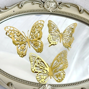 Three golden hollow metal butterflies displayed on a vintage carved mirror frame