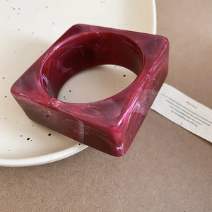 Detail of red marble texture acrylic square bangle resting on a ceramic plate