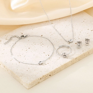 Elegant stainless steel jewelry set with flower charms on a beige stone background