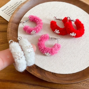 Close-up of fluffy C-shaped earrings with snowflake pendants in pink, red and white